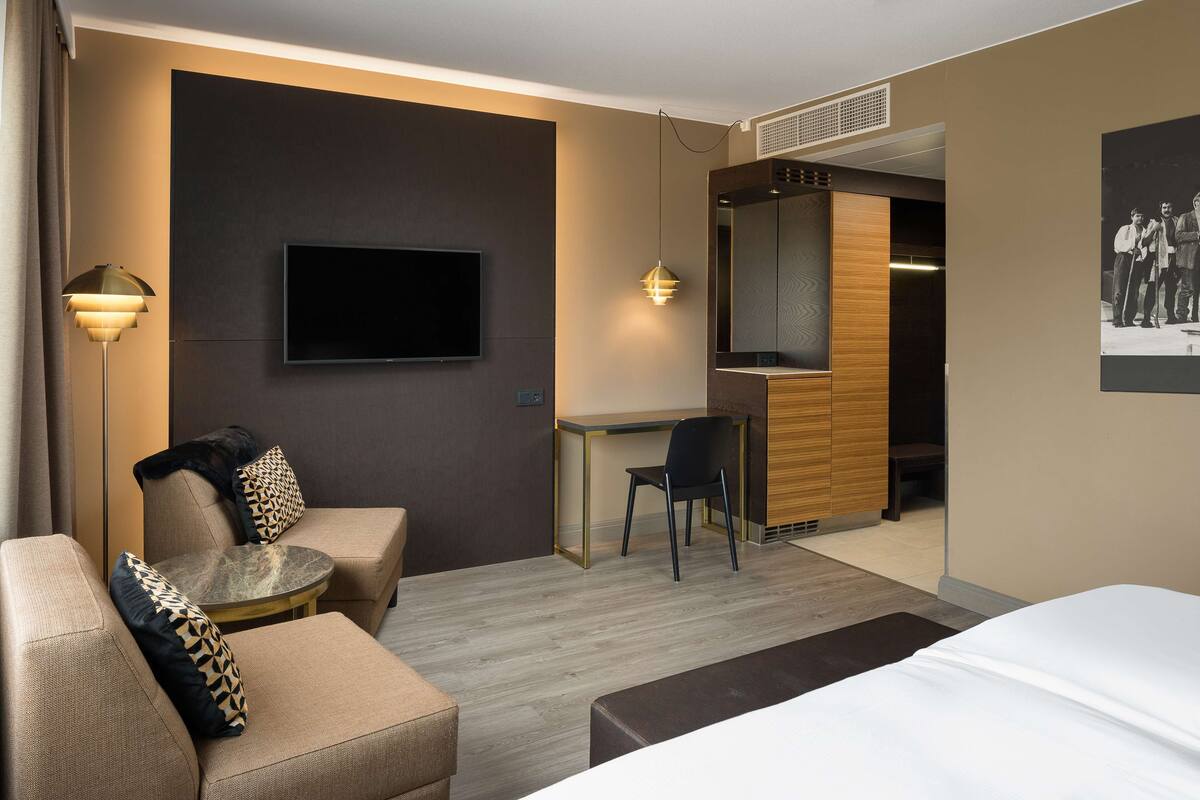 Ein modernes Hotelzimmer mit Bett, einer Sitzecke, einem Schreibtisch und einem Sessel.