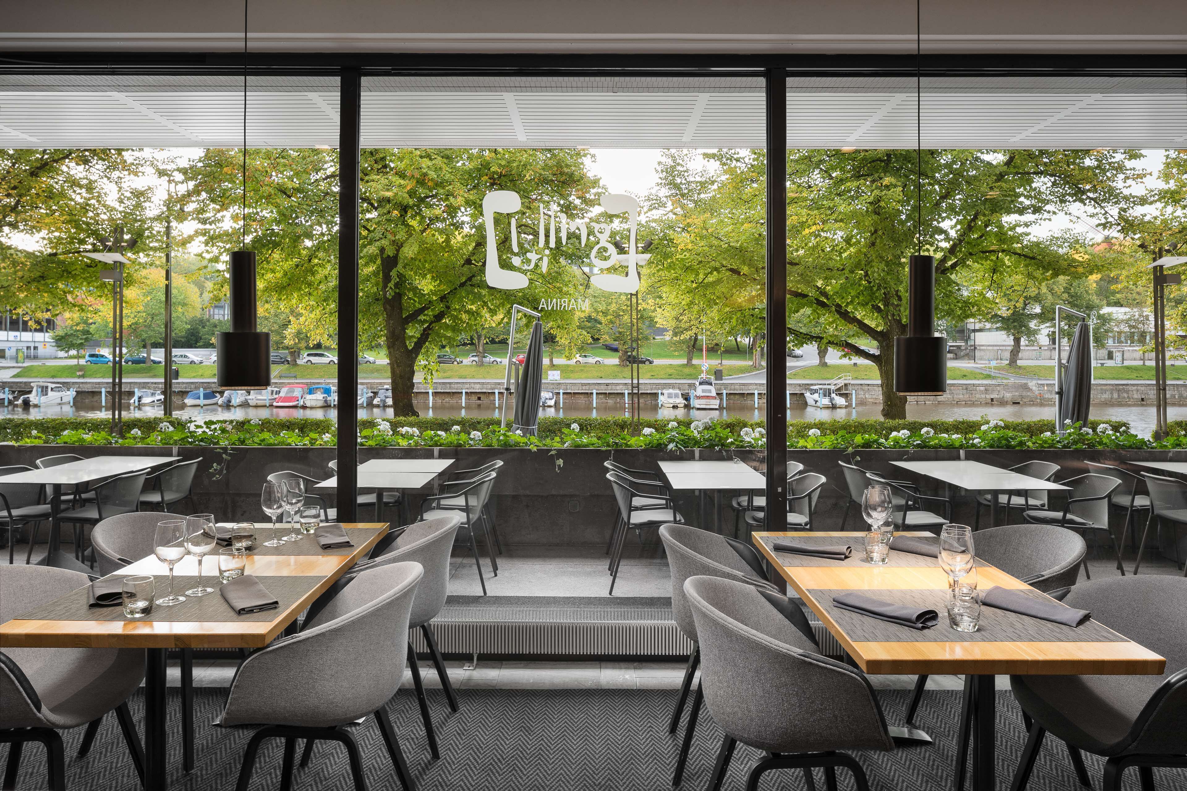An outdoor dining area with tables and chairs, large windows, and a view of a park and street.