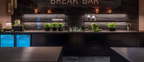 A modern break bar with a marble backsplash, glass shelves, and a sleek black countertop.