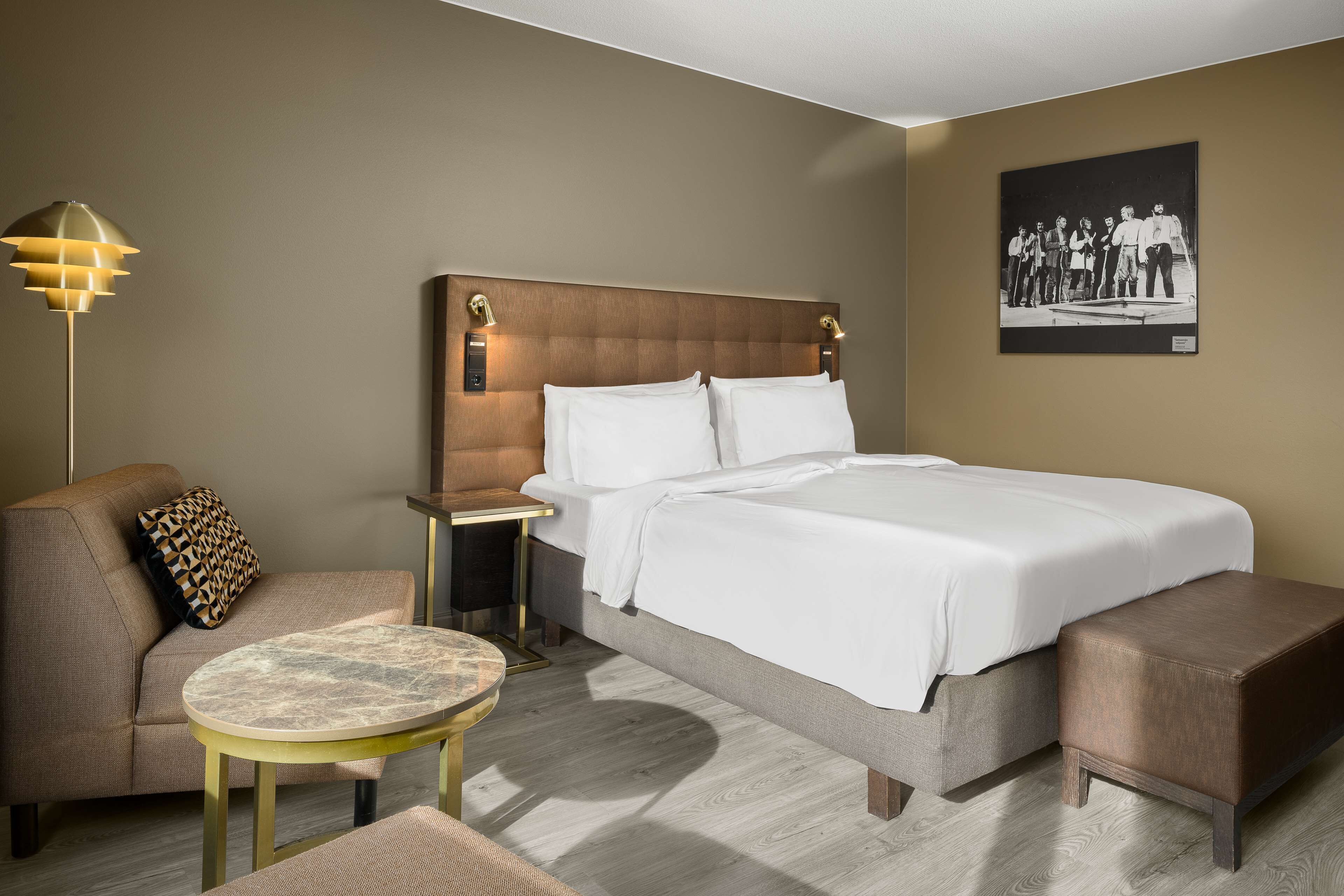 A hotel room with a bed, a sofa, a small table, and a nightstand.
