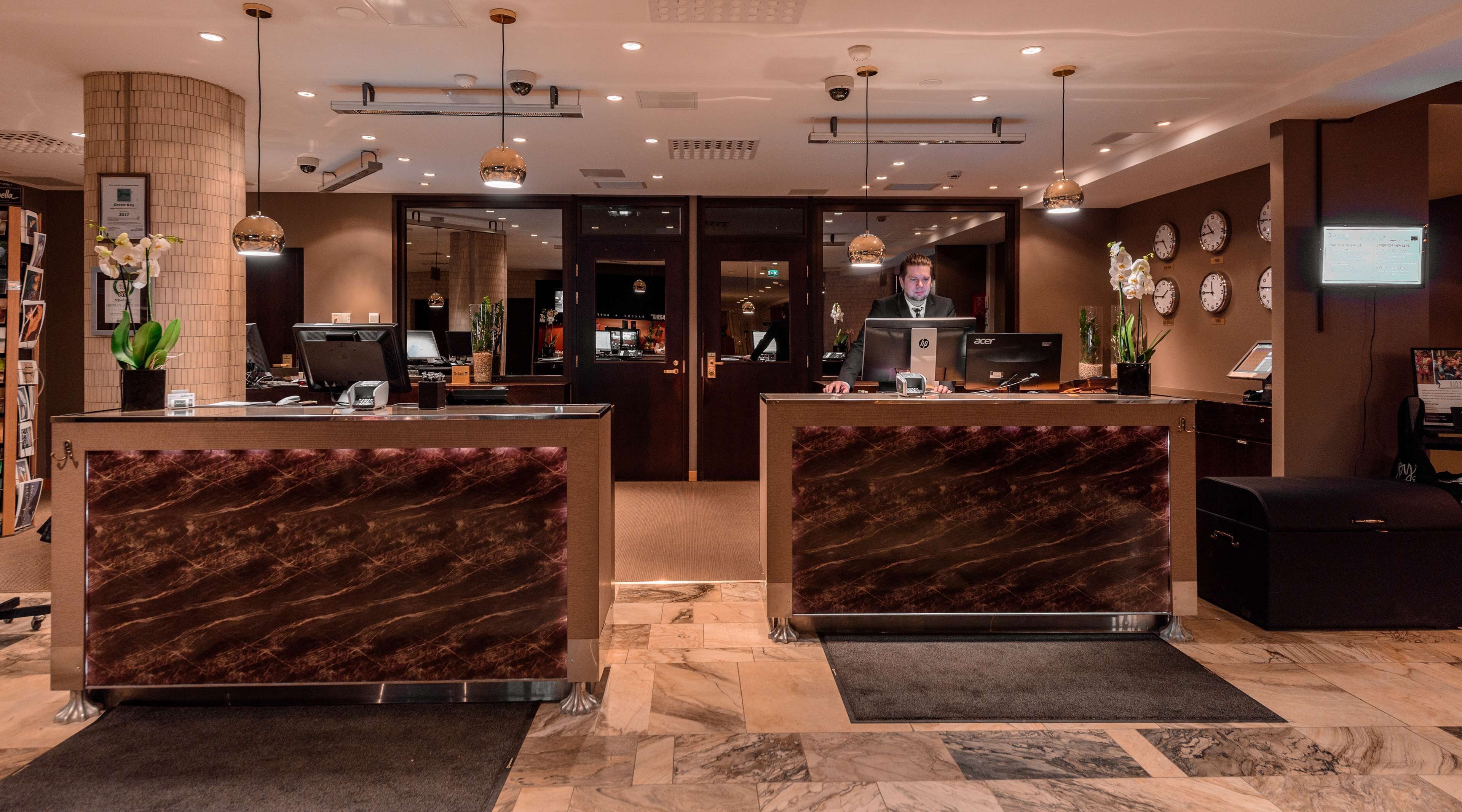 A hotel reception area with marble reception desks, a digital clock, and a security camera.