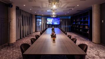 A conference room with a long table, chairs, a projector screen, and a bookshelf.