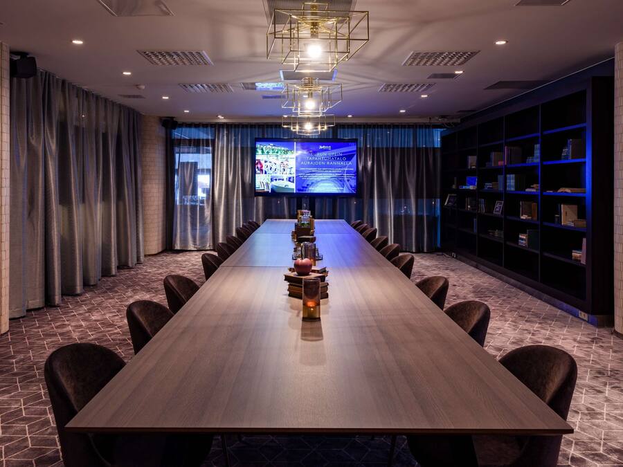 A conference room with a long table, chairs, a projector screen, and a bookshelf.