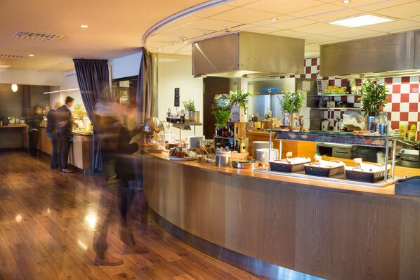 Un restaurant doté d’un comptoir en bois, d’un espace bar et d’une cuisine visible à travers une paroi en verre.