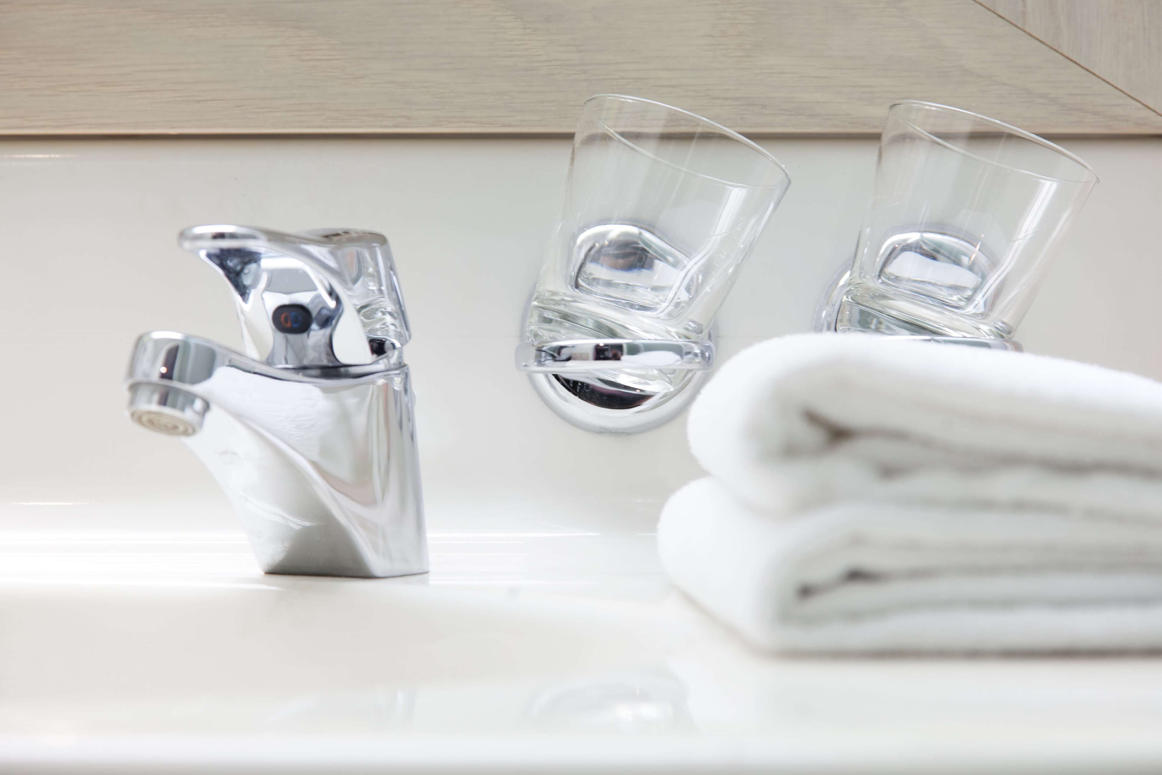 Een badkamer met een moderne kraan, twee glazen en een stapel witte handdoeken.