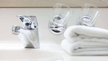 Een badkamer met een moderne kraan, twee glazen en een stapel witte handdoeken.