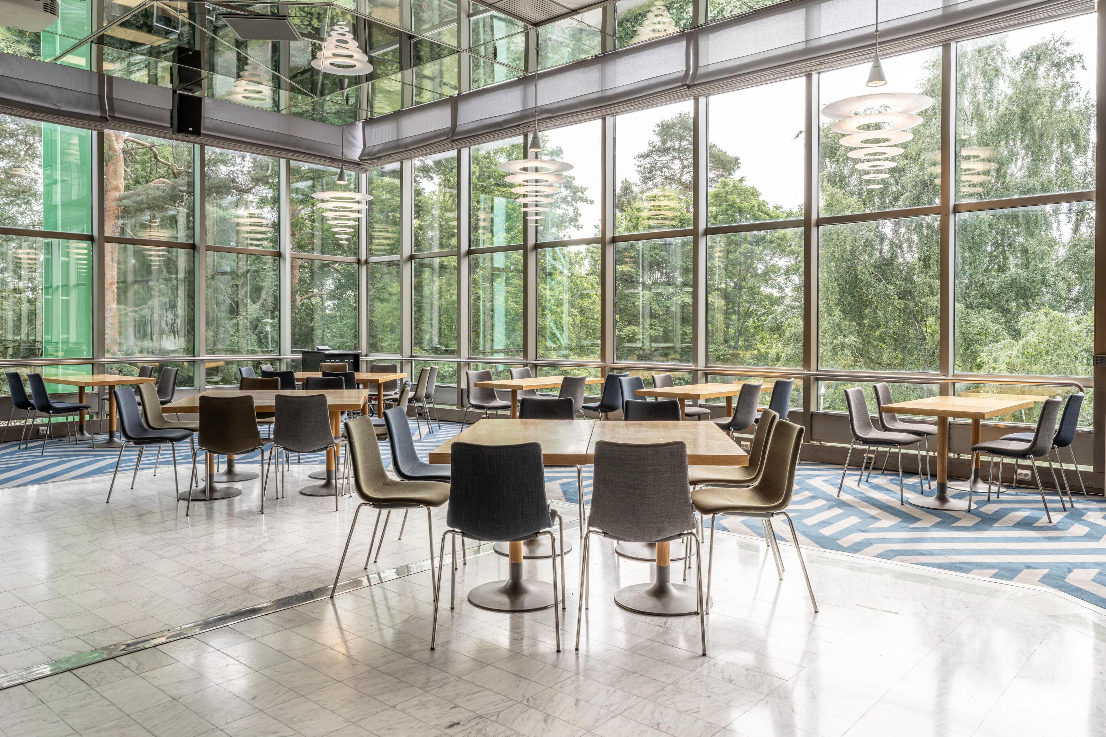 A spacious indoor area with large windows, multiple tables and chairs, and hanging pendant lights.