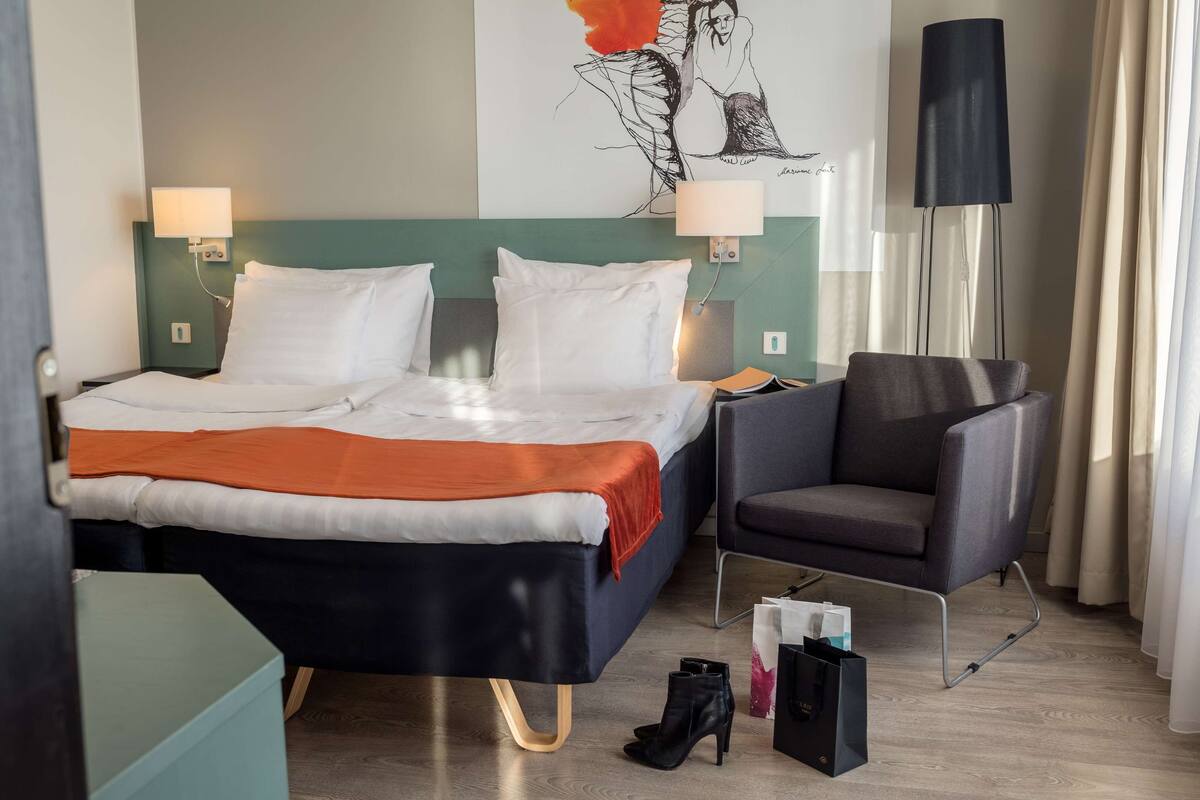 A hotel room with a bed, a chair, a lamp, and a floor lamp.