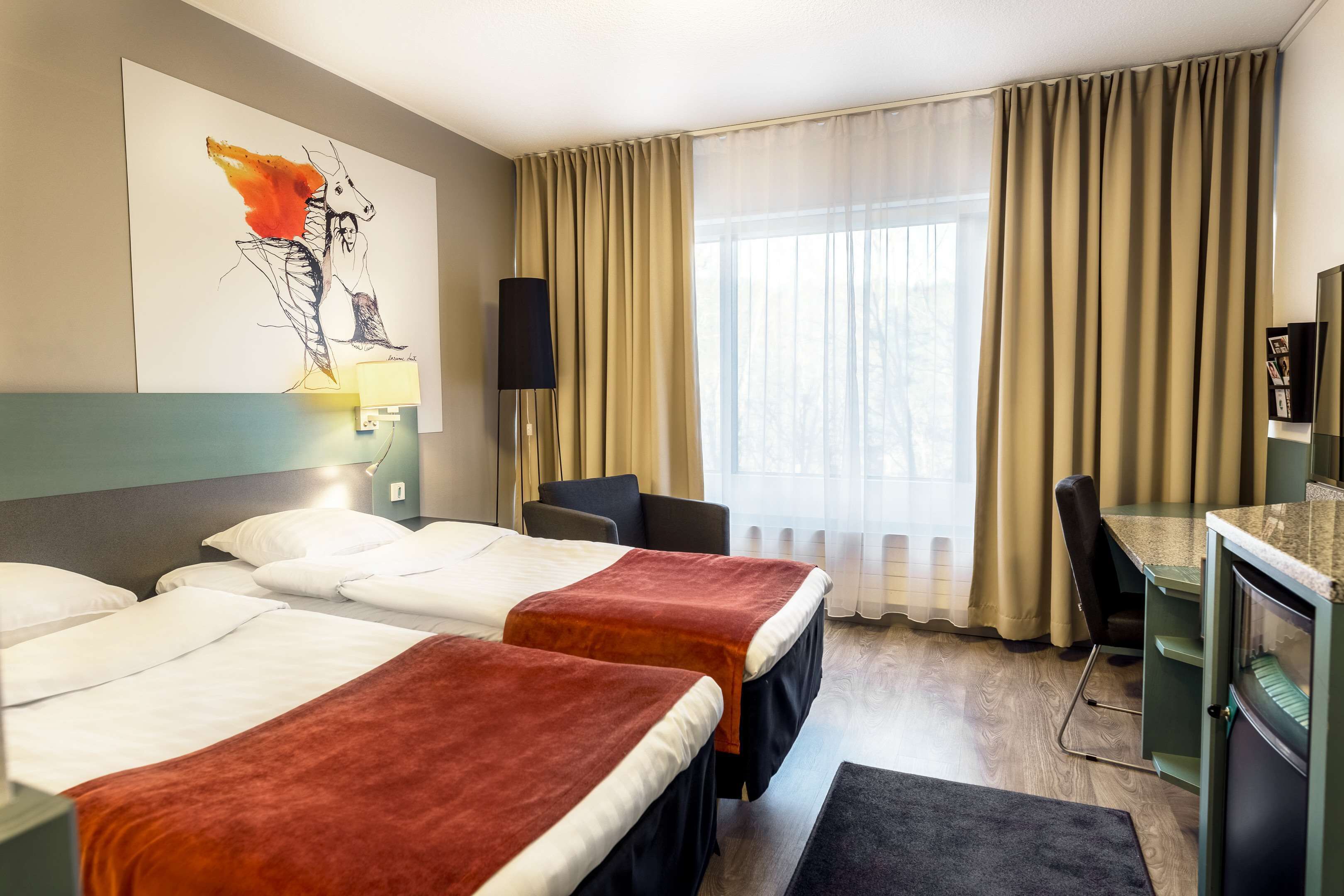 Una habitación de hotel con dos camas, un escritorio, una silla, una lámpara y un cuadro en la pared.