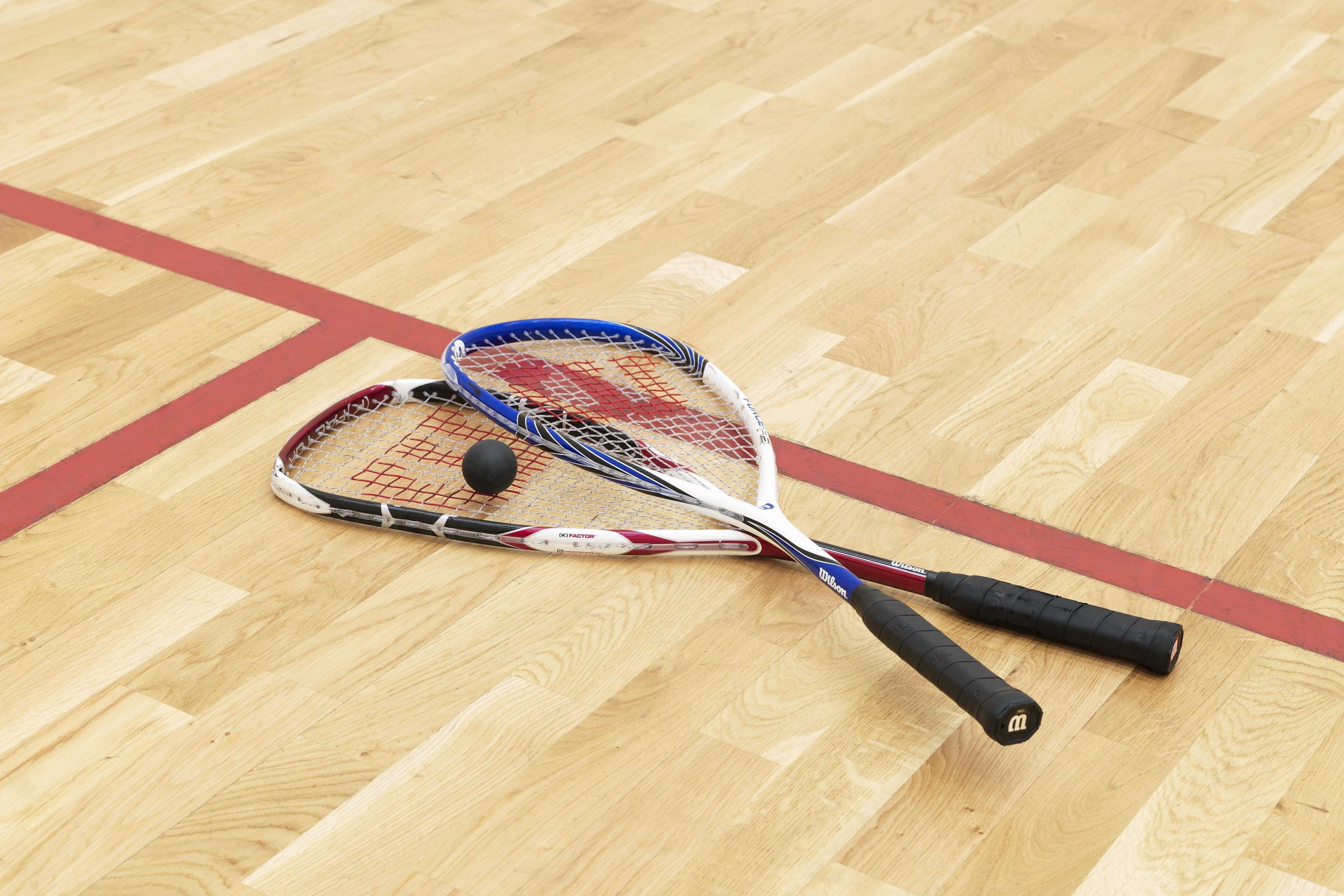 Deux raquettes de tennis sur un plancher en bois, avec des lignes rouges.
