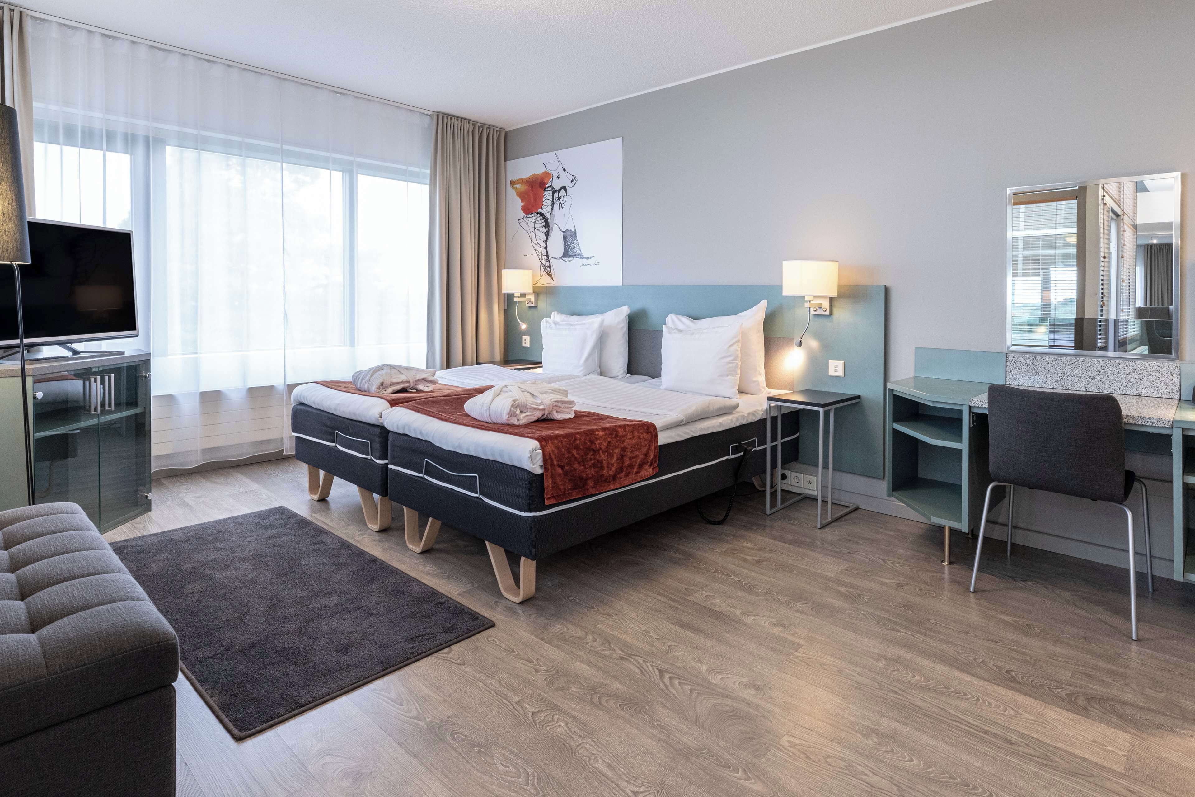 Een moderne hotelkamer met een groot bed, een bureau, een stoel, een televisie en een schilderij aan de muur.