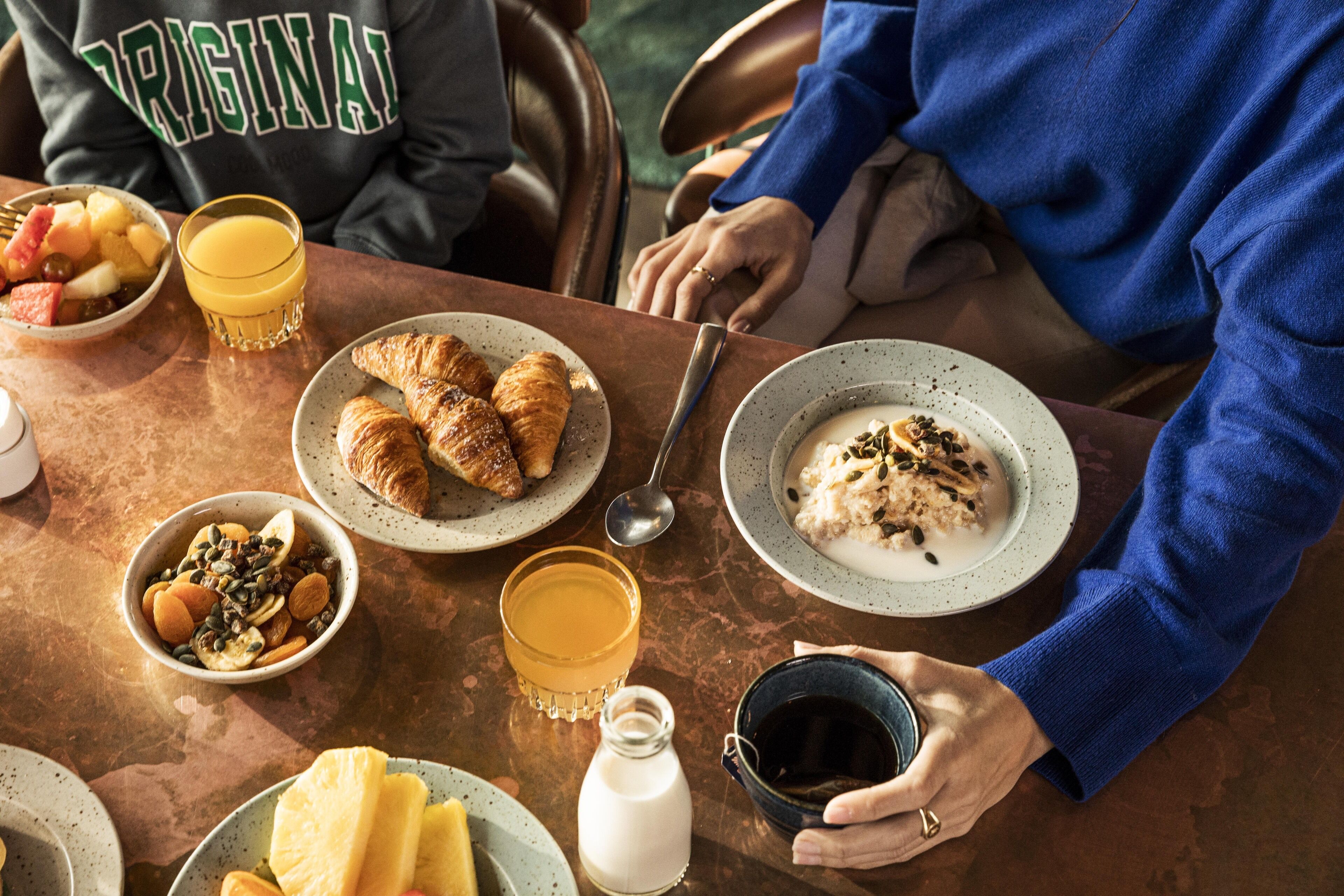 Een ontbijt met croissants, fruit en een glas sinaasappelsap op een tafel.