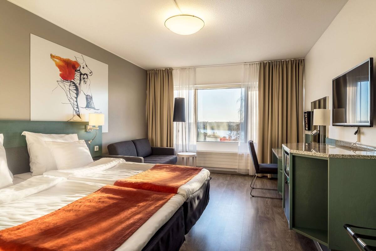 A hotel room with a bed, a desk, a chair, a TV, and a window with curtains.