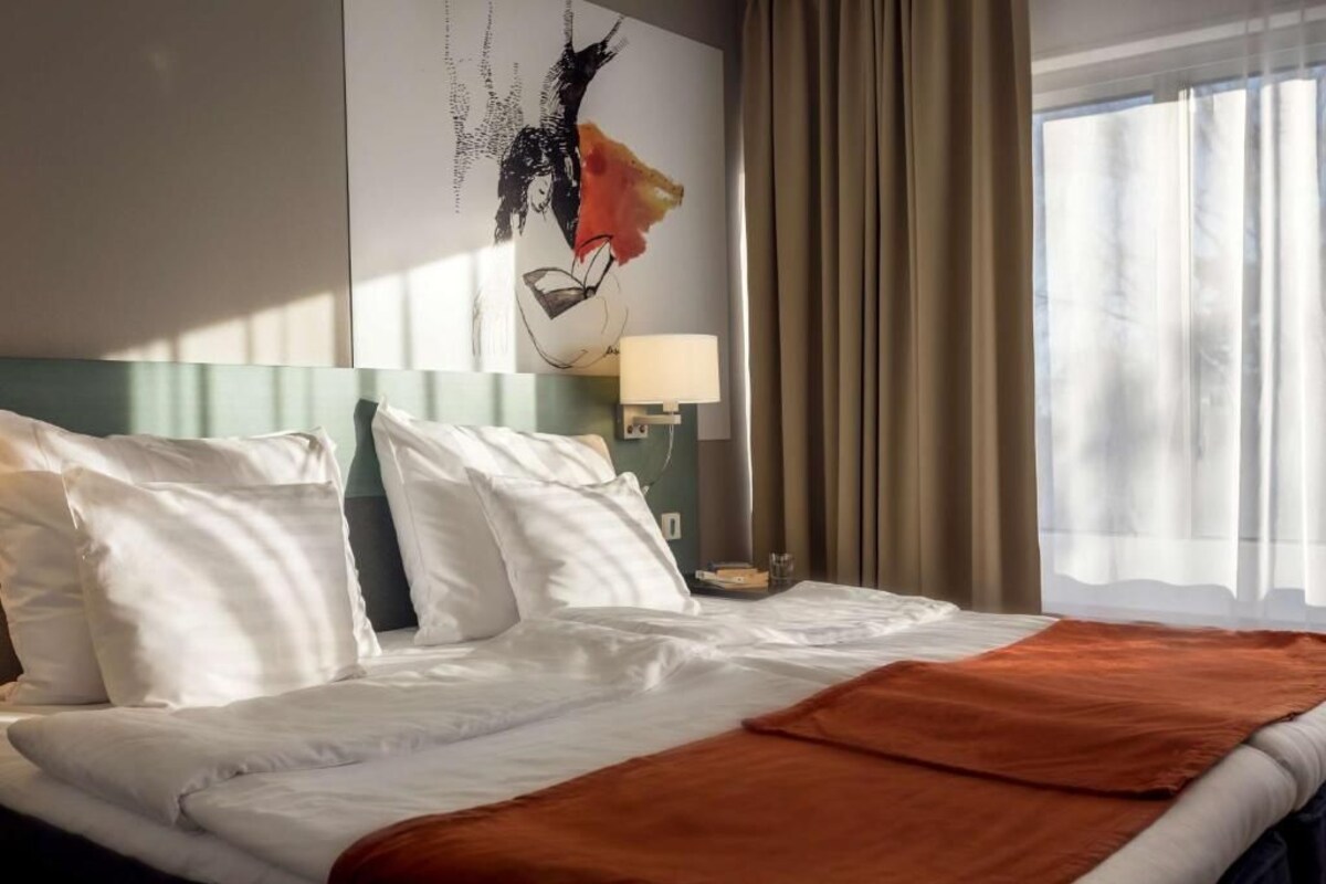 A hotel room with a bed, a nightstand, a lamp, and a window with curtains.