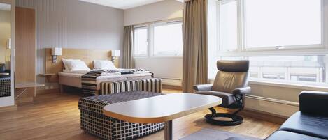 A modern hotel room with a bed, a sofa, a dining table, and a chair.