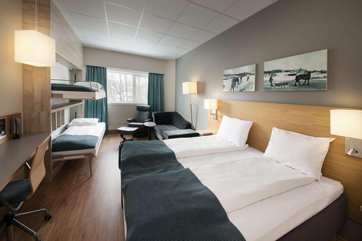 A hotel room with two beds, a desk, a chair, a small table, and a window with curtains.