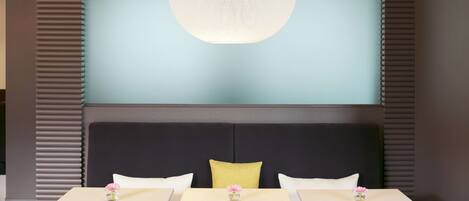 Una habitación de hotel moderna con una lámpara redonda grande, un sofá con tres almohadas y una mesa con dos sillas.