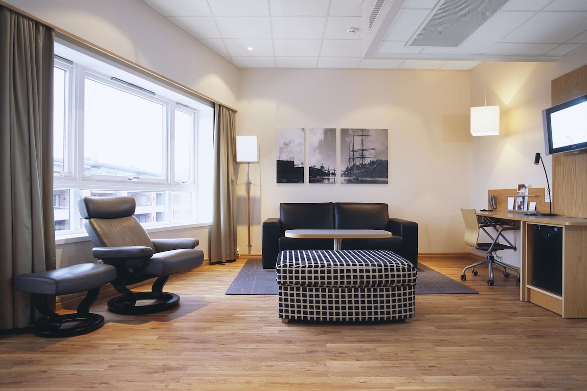 Una habitación de hotel moderna con sofá, una silla, una mesita y televisión.