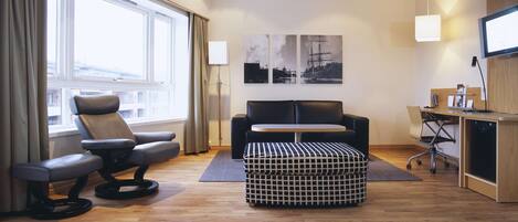 Una habitación de hotel moderna con sofá, una silla, una mesita y televisión.