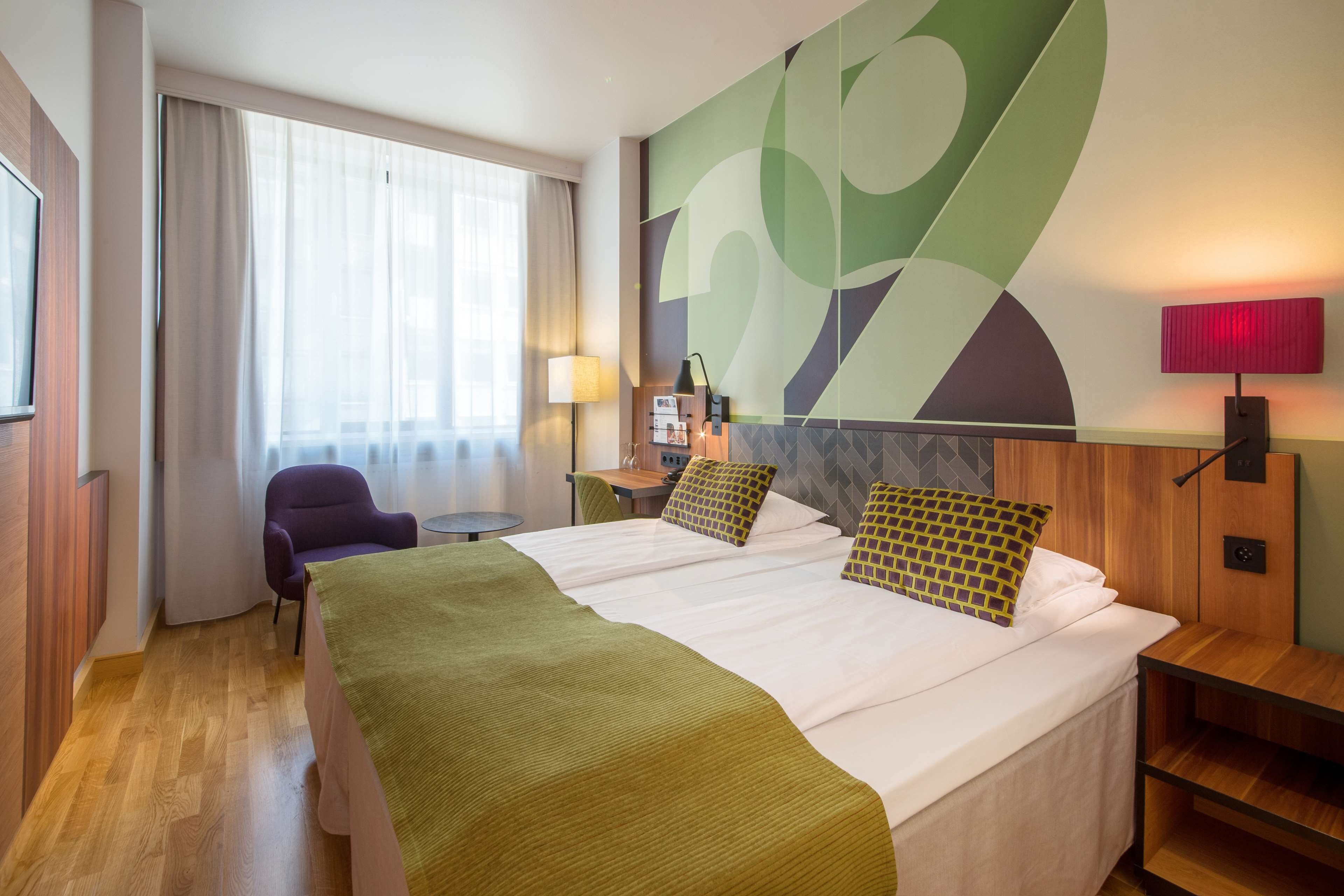 Une chambre d’hôtel avec un grand lit, un bureau, une chaise, une télévision et un grand élément de décoration murale abstrait.