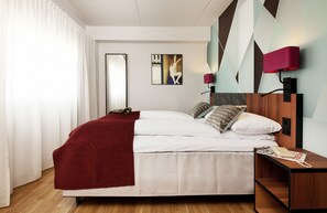 A modern hotel room with a large bed, a wooden nightstand, a red lamp, and a geometric wall design. - Scandic Solli Oslo (Oslo)