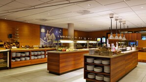 A modern restaurant with a central island, wooden paneling, and a variety of dishes displayed on shelves. - Scandic Solli Oslo (Oslo)