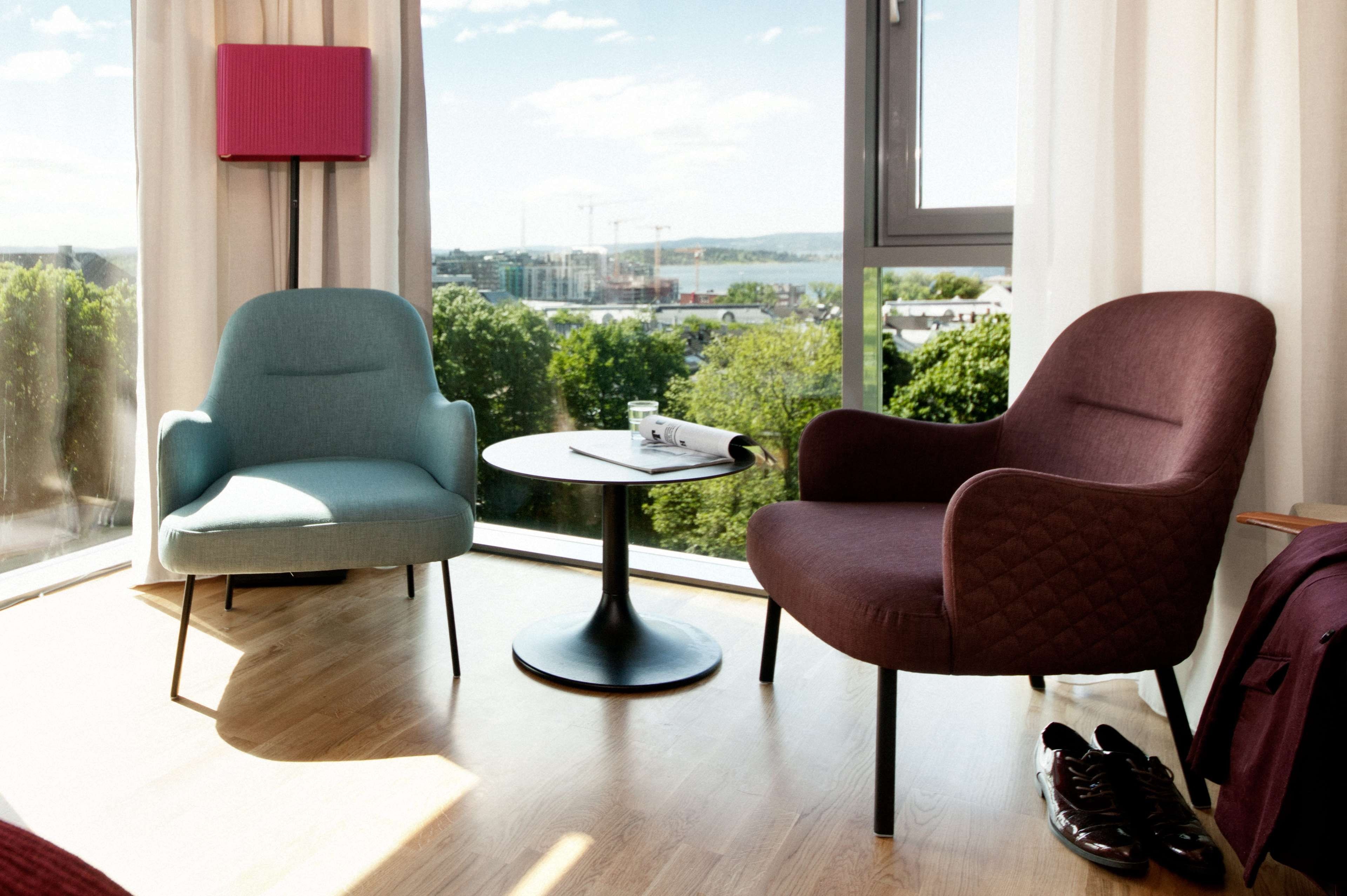 A modern room with two chairs, a small table, and a view of a cityscape through large windows.