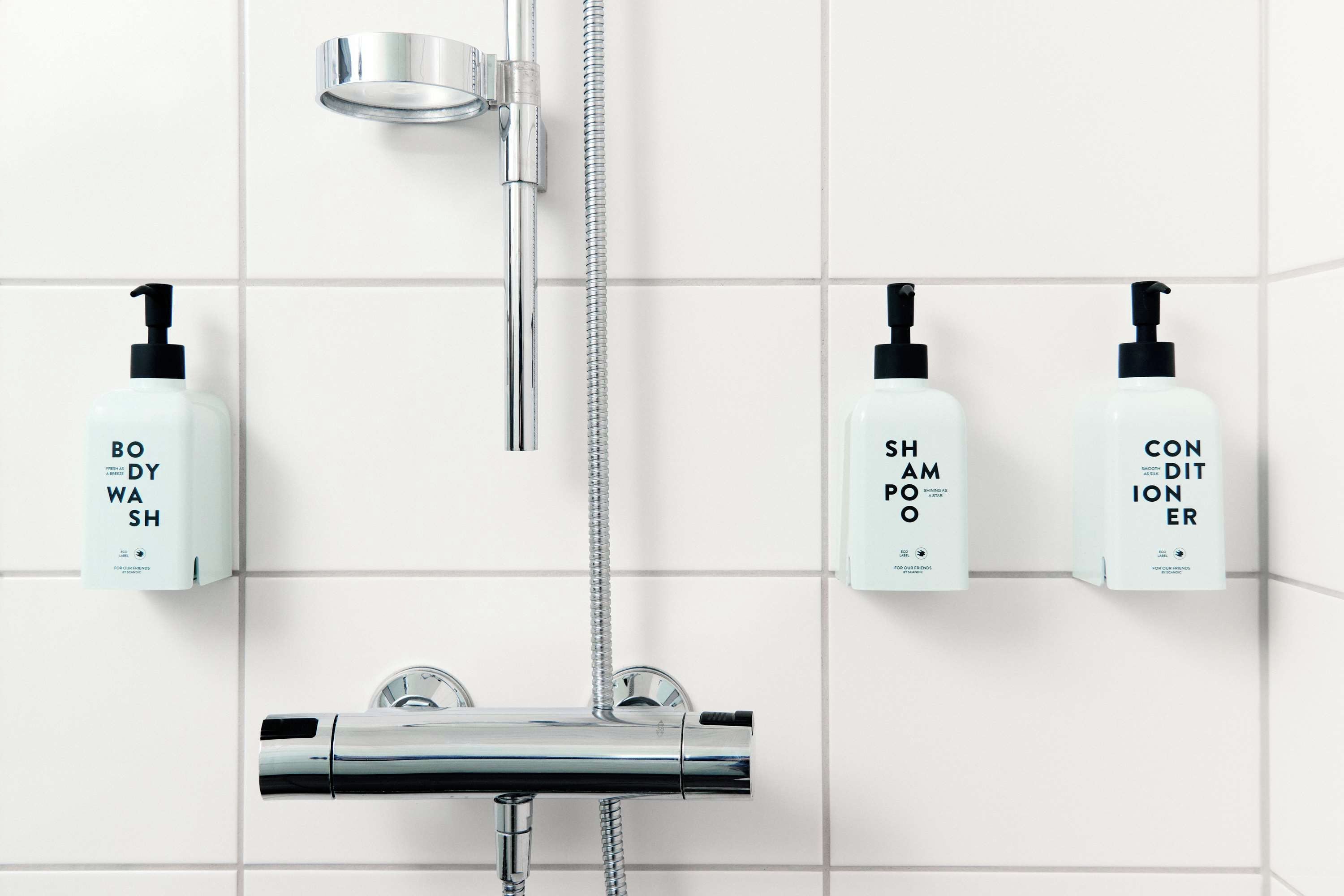 A bathroom with a chrome showerhead, a handheld showerhead, and three bottles of toiletries on the wall.