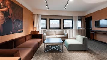 A modern living room with a brown sofa, a beige sofa, a grey sofa, a small table, and a TV on the right.