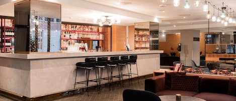 Una zona de bar con barra, varios taburetes altos y un área de estar con una mesa redonda y sofás.