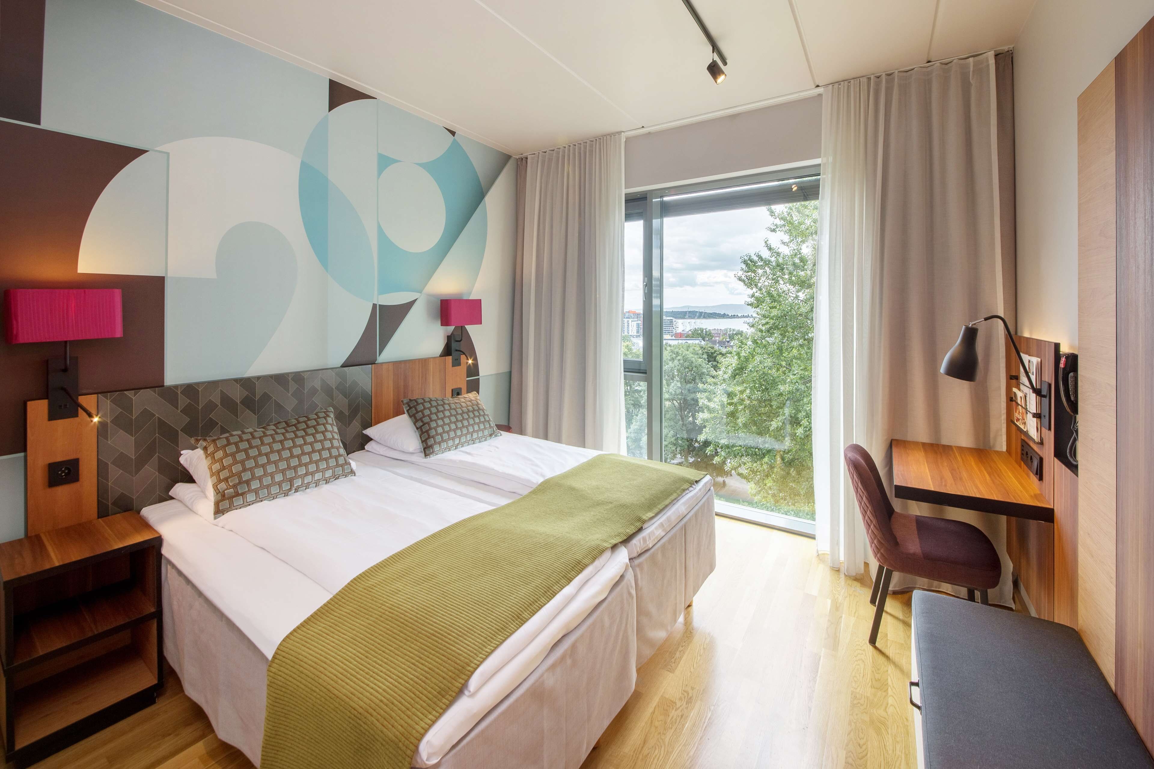 A modern hotel room with a large bed, a desk, and a chair.