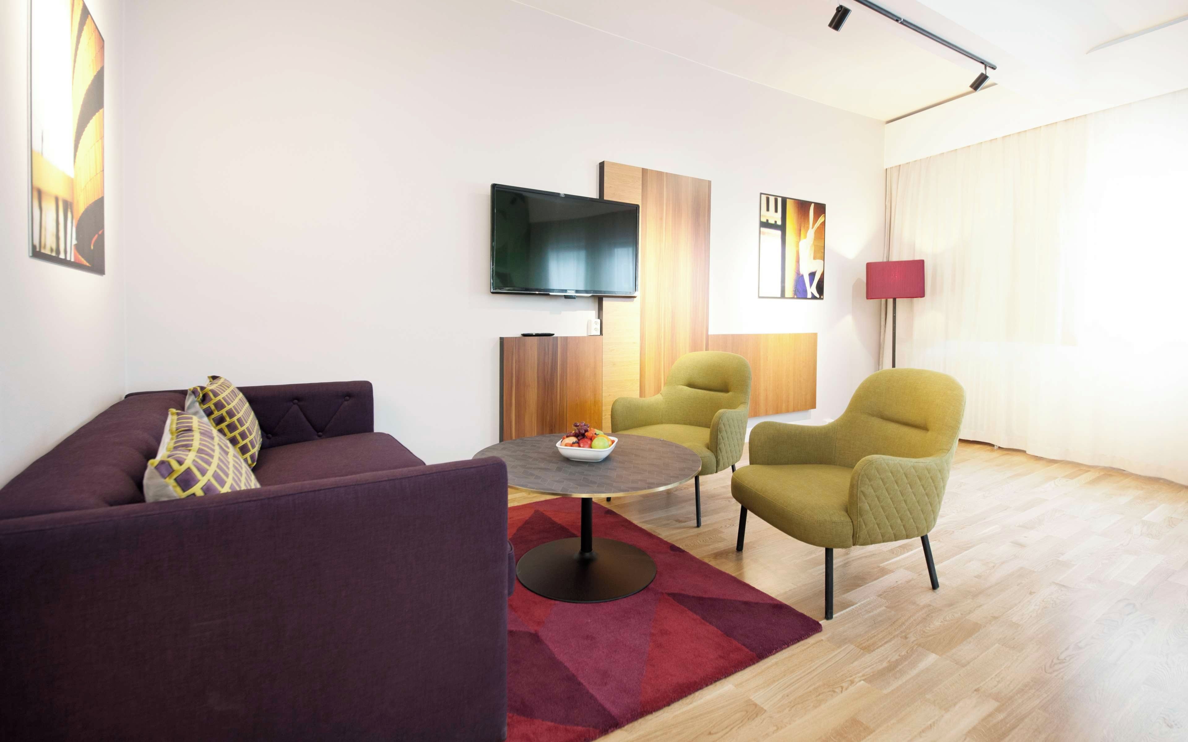 Un salon moderne comprenant un canapé, deux fauteuils, une table basse et un téléviseur à écran plat fixé au mur.