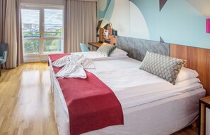 A hotel room with a large bed, a desk, a chair, and a view of the city through the window. - Scandic Solli Oslo (Oslo)