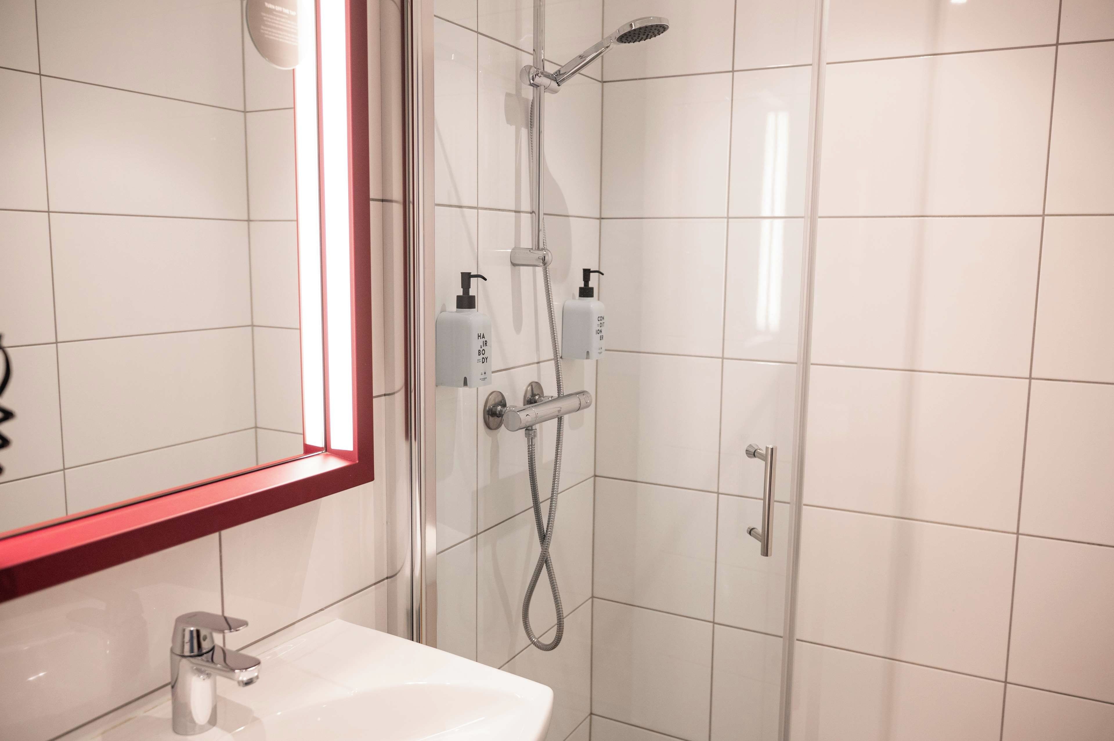 Un bagno moderno con box doccia in vetro, lavandino bianco e specchio con cornice rossa.