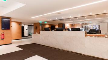 Una moderna zona de recepción de hotel con un mostrador de mármol, un reloj digital y un extintor.