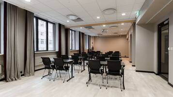 Un salón de conferencias con filas de mesas y sillas, ventanas amplias y una decoración en tonos neutros.