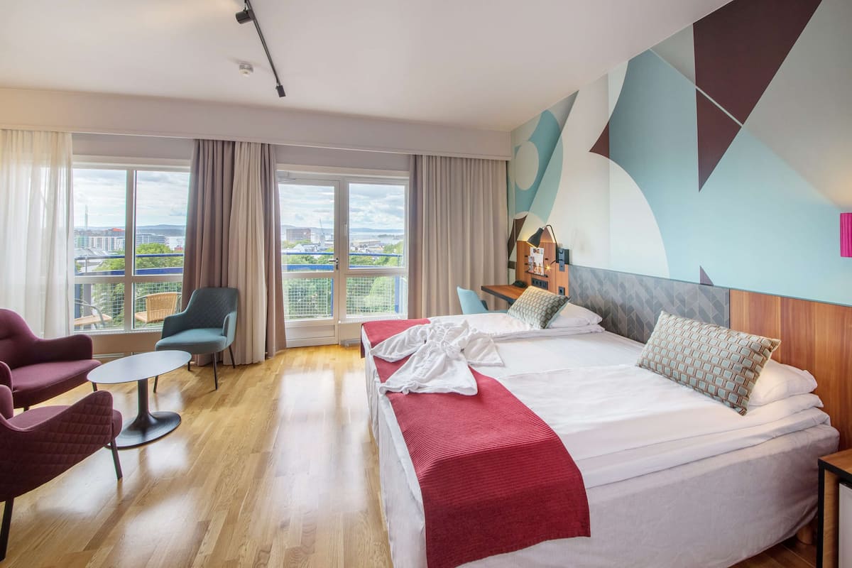 A hotel room with a large bed, a desk, a chair, and a view of the city.