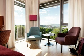 A modern hotel room with a large window, a round table, two chairs, a bed, and a red quilted chair. - Scandic Solli Oslo (Oslo)