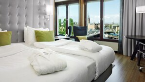 A hotel room with a large bed, a chair, a table, and a view of a cityscape through large windows. - Hilton Stockholm Slussen (Stockholm)