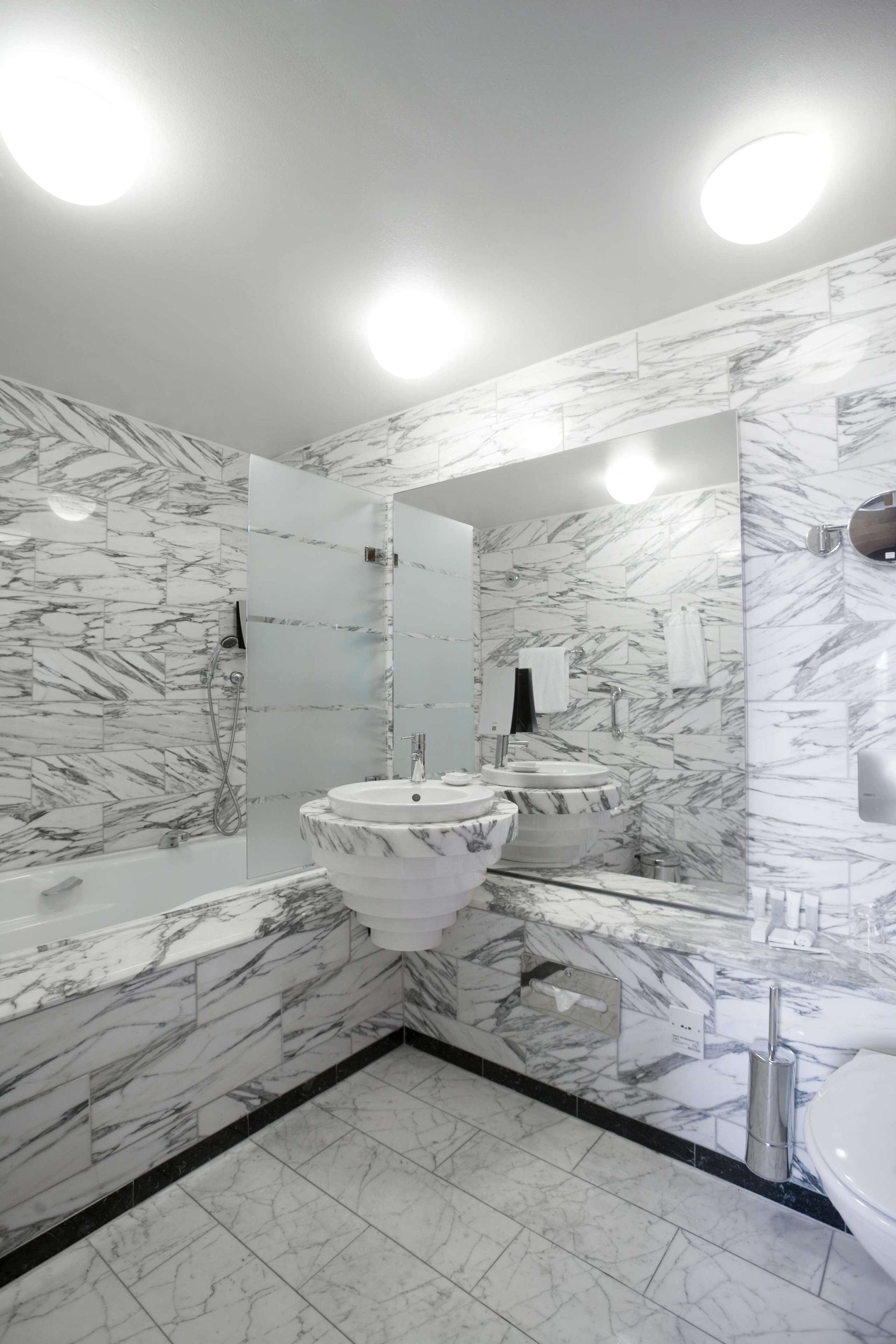 A modern bathroom with marble walls and a large mirror.