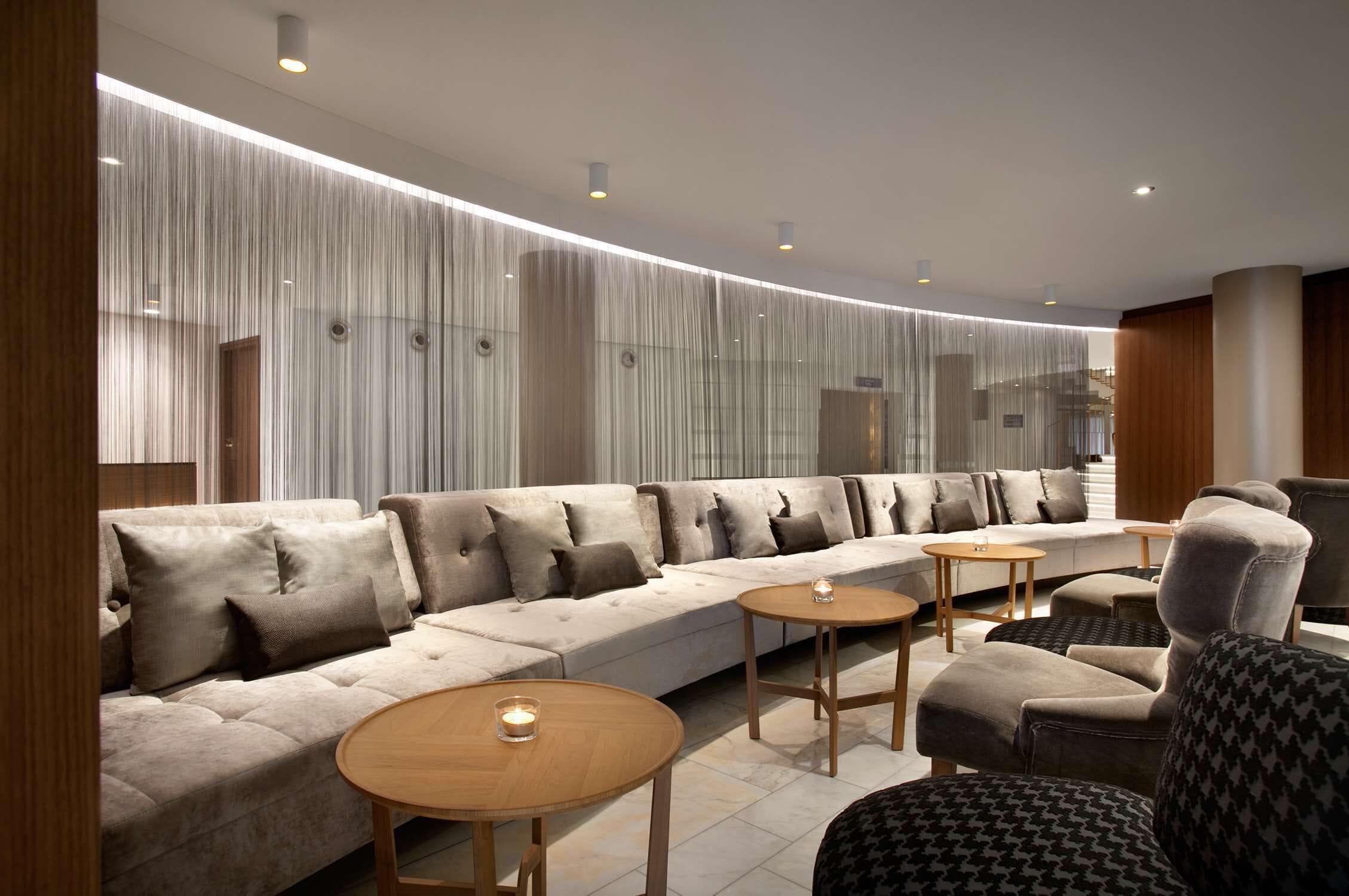 Un espace de détente moderne comprenant un canapé, des fauteuils et de petites tables, avec un design épuré et contemporain et un éclairage d’ambiance.