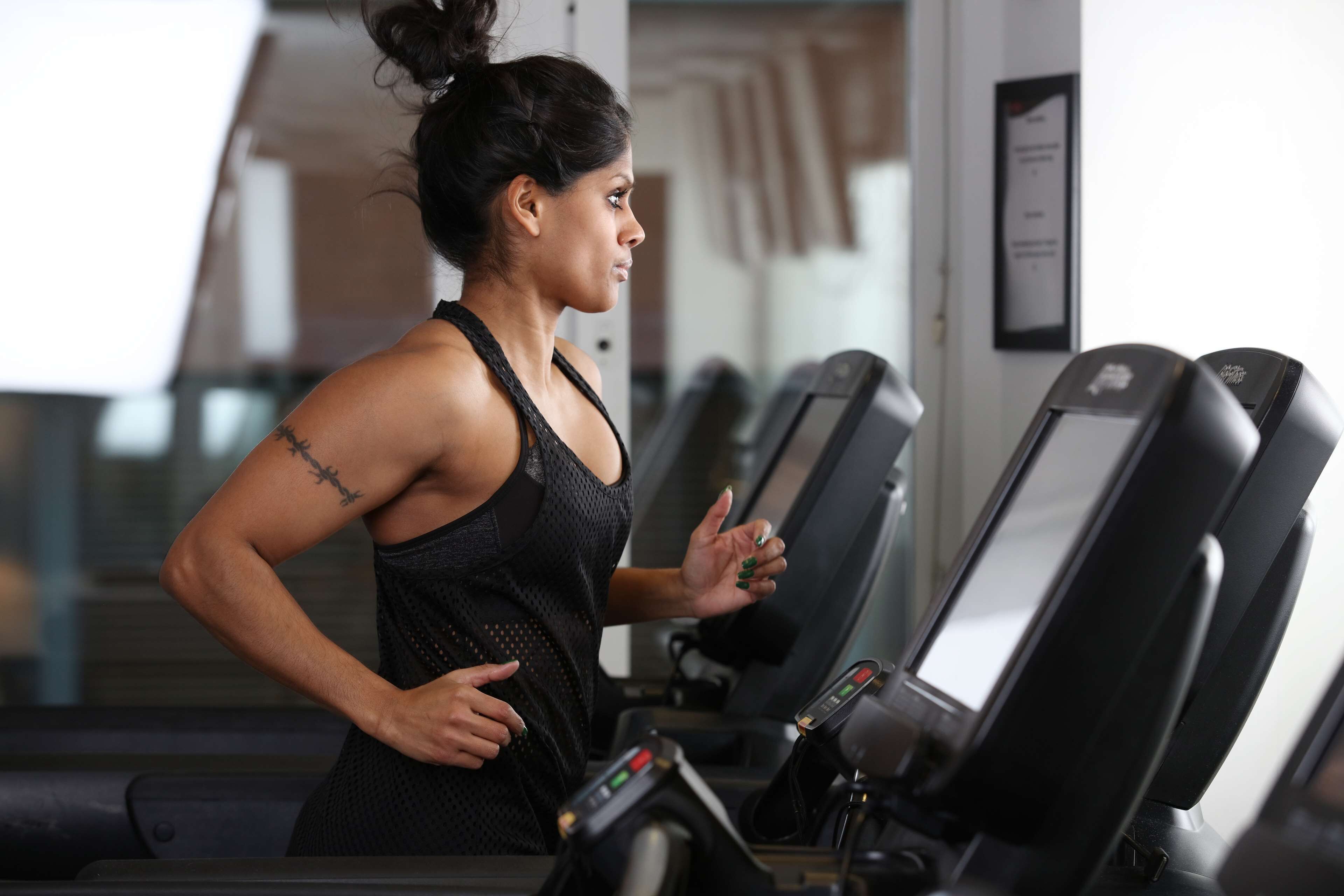 A person running on a treadmill in a gym with multiple treadmills and a wall-mounted sign.