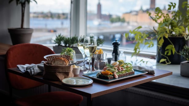 A dining table with a meal, glasses, and a view of a cityscape through a window. - Hilton Stockholm Slussen (Stockholm)