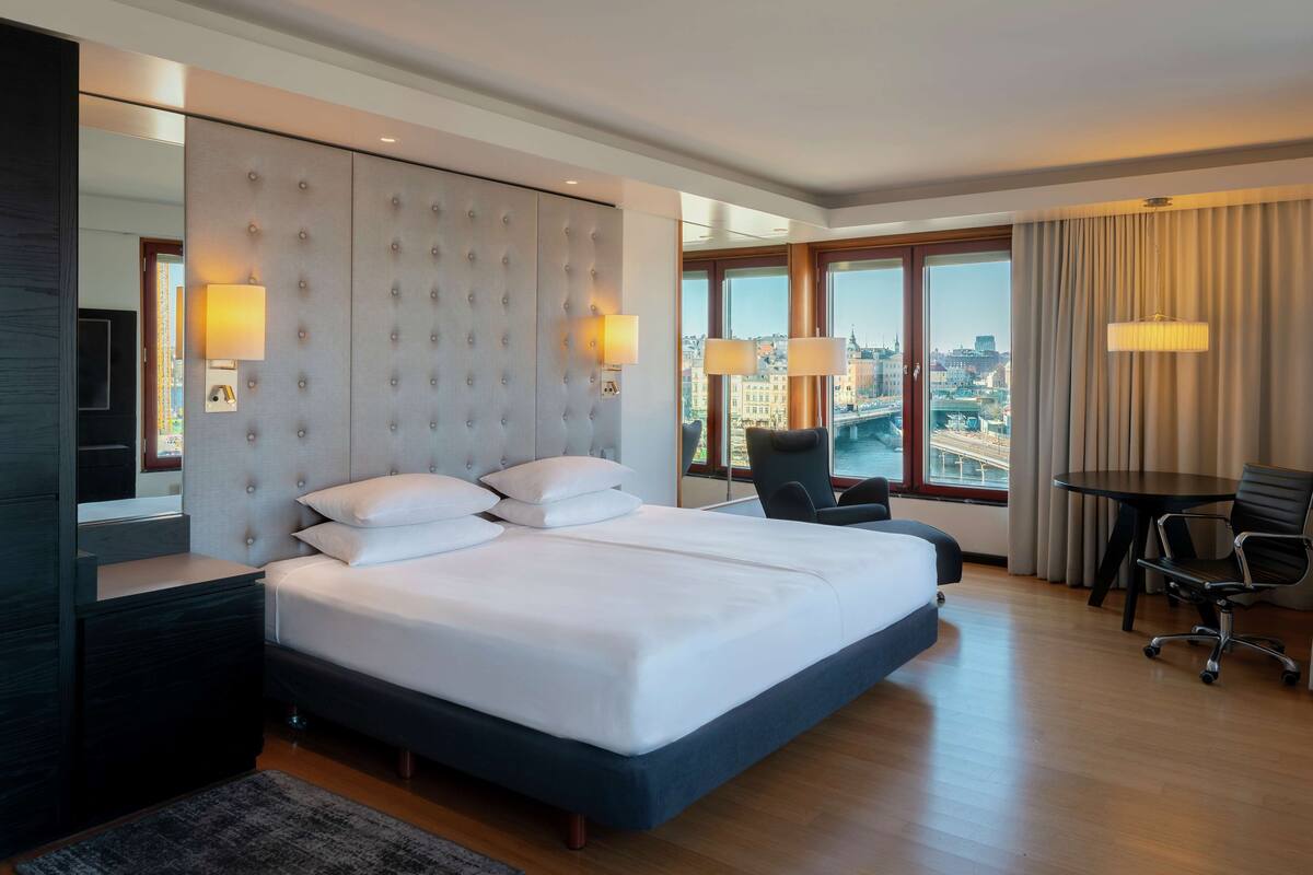 A modern hotel room with a large bed, a desk, and a chair.