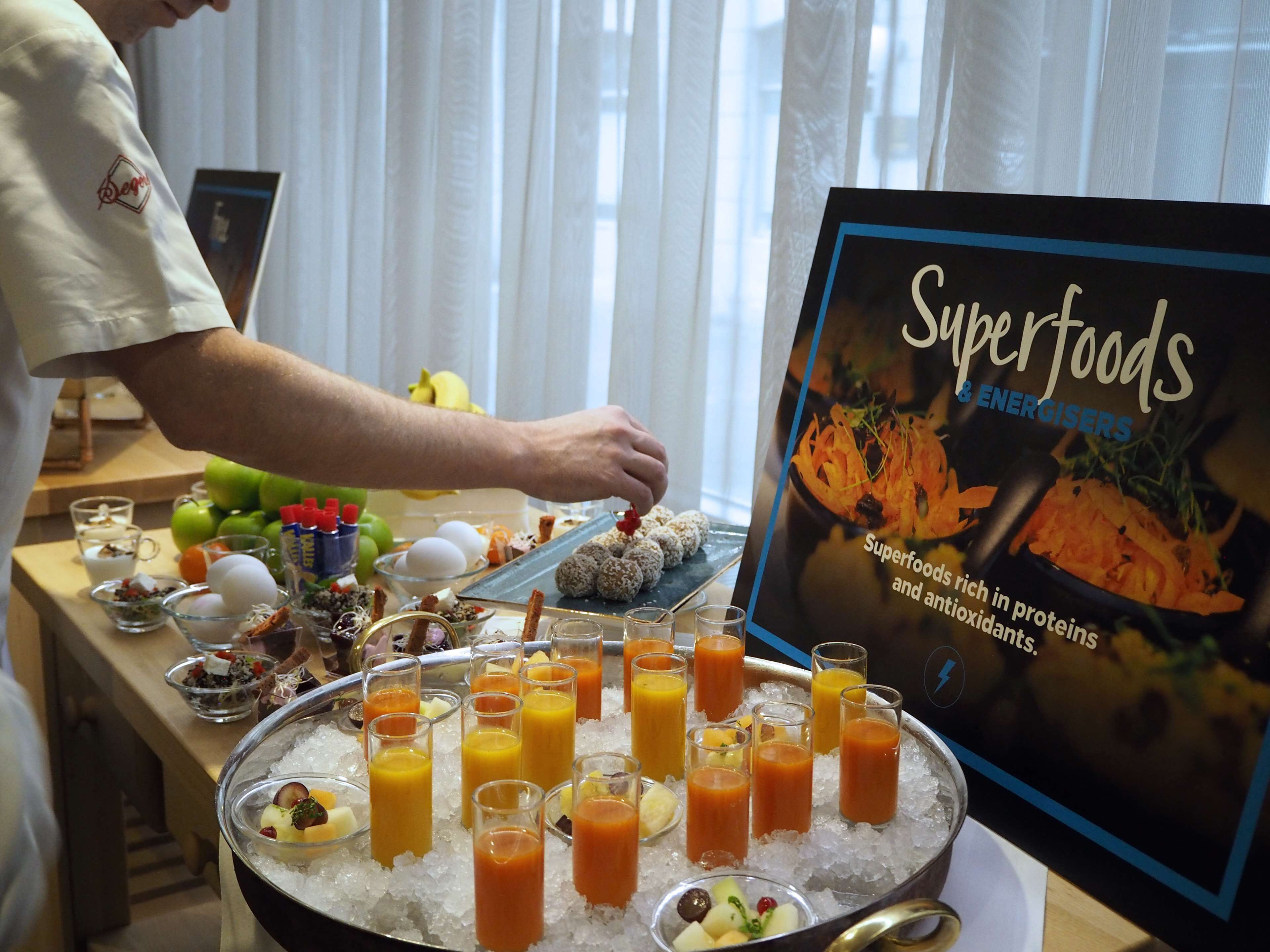 Ein reichhaltiges Buffet mit verschiedenen Speisen und einem Schild mit der Aufschrift 'Superfoods & Energisers'.