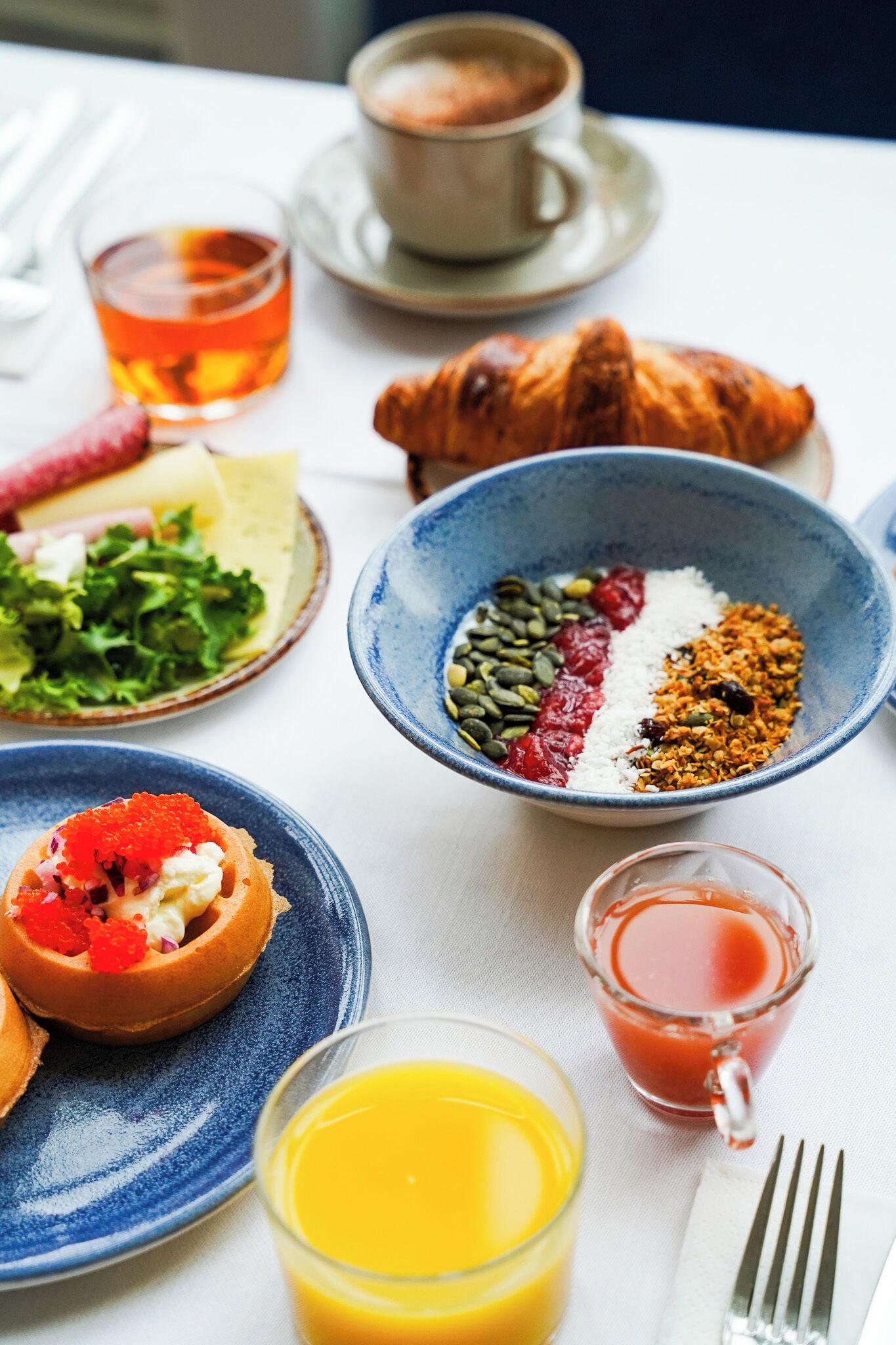 Une table mise pour le petit-déjeuner avec des croissants, un bol de céréales, un verre de jus d’orange et une tasse de thé.