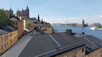 Une vue urbaine avec des bâtiments le long d’une rivière, dont une église imposante dotée d’un dôme vert et de flèches.