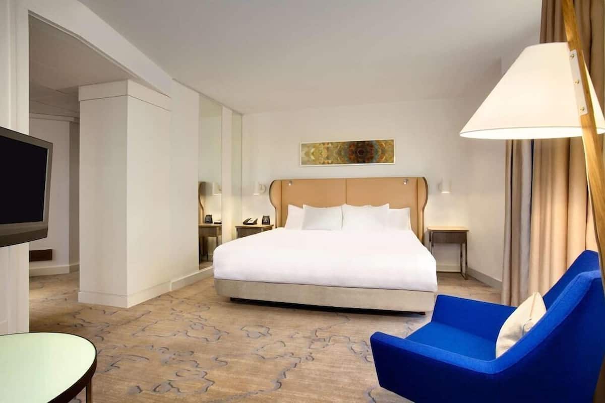 A hotel room with a large bed, a TV, a desk, a chair, and a lamp.