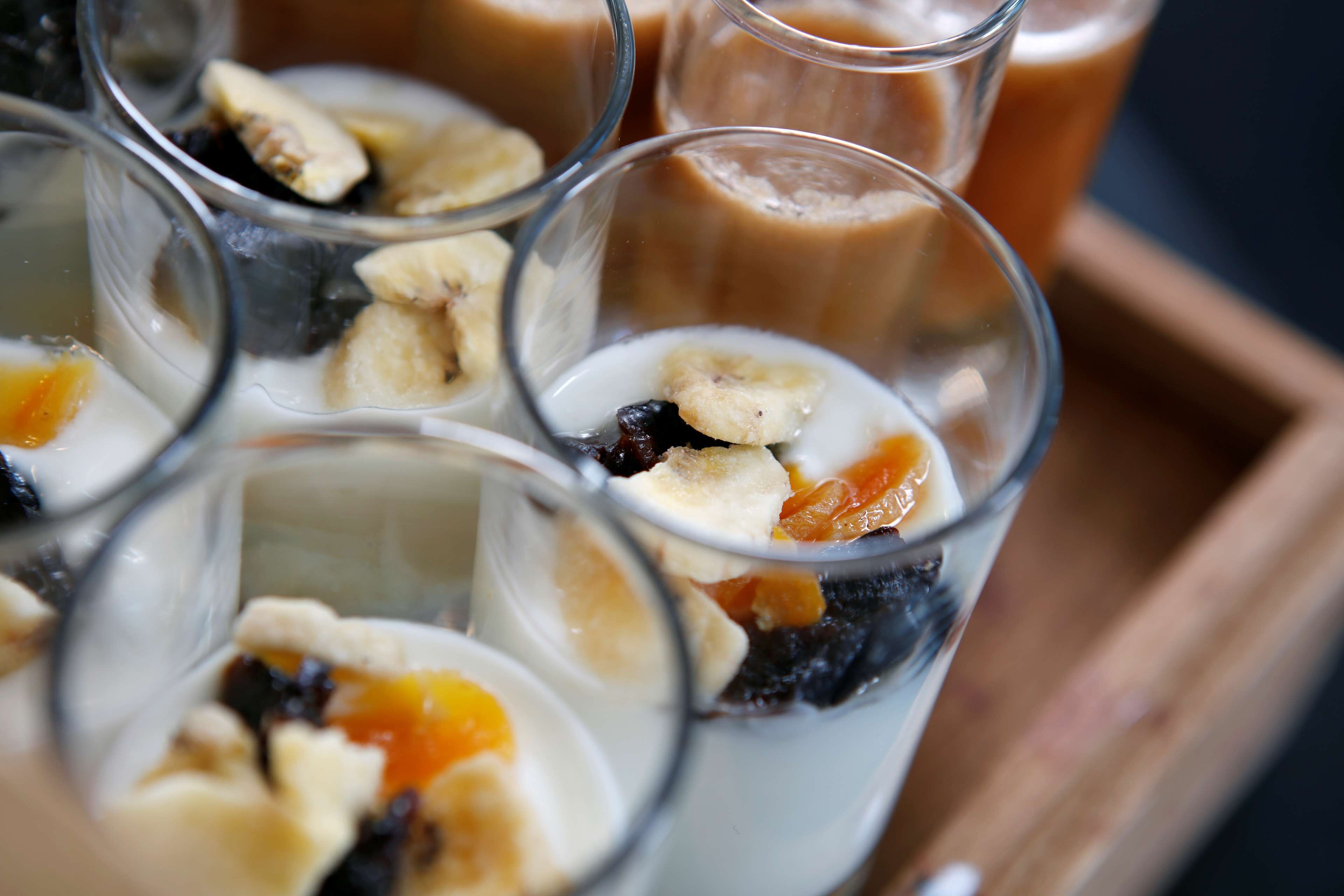 A tray with several glasses containing a dessert with fruits and a creamy liquid.