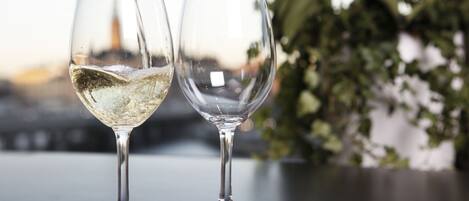 Two wine glasses on a table with a blurred background of greenery and a building.